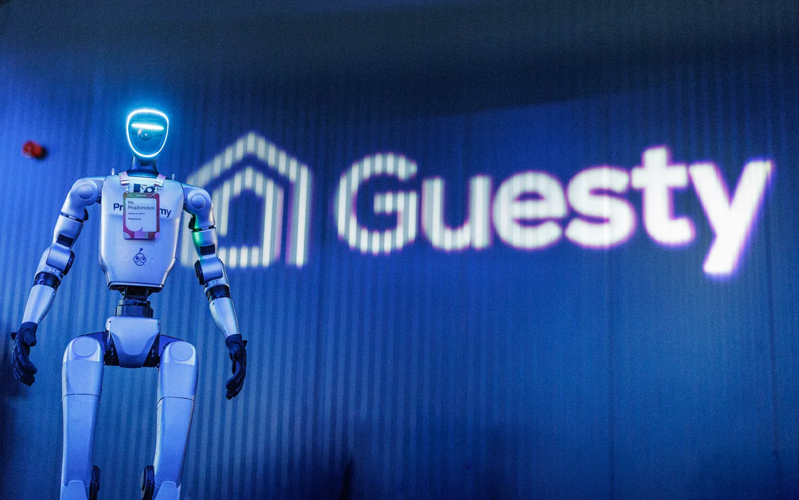 Proptonobot standing in front of the illuminated Guesty logo